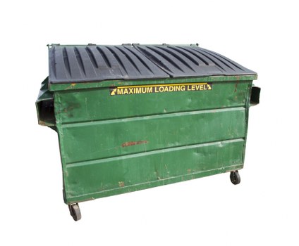 A large, rectangular green metal dumpster with a black, textured hinged lid and visible signs of wear and rust, situated outdoors on a paved surface. The dumpster has four small caster wheels at the base, allowing for mobility, and features prominent yellow text indicating a maximum loading level. The environment appears to be an outdoor commercial or warehouse area, with part of a concrete or tarmac surface visible. The scene suggests it is ready for rubbish collection or waste removal, as would be typical for a professional waste management service in Wimbledon or nearby areas, supporting services offered by Commercial Waste Removal Wimbledon.